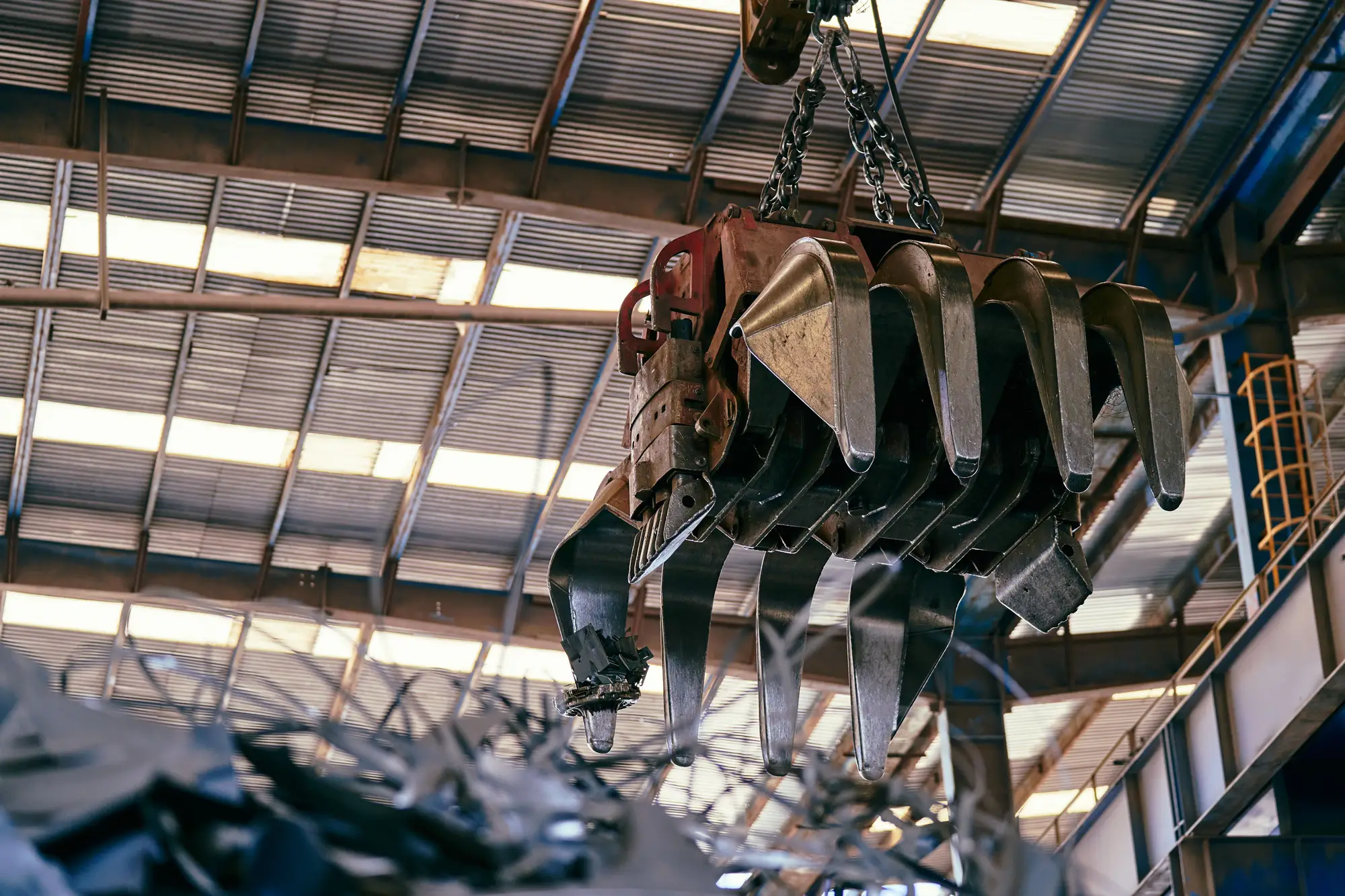 Scrap metal heaped under the roof of a steel-framed shed, a crane grab hanging over it