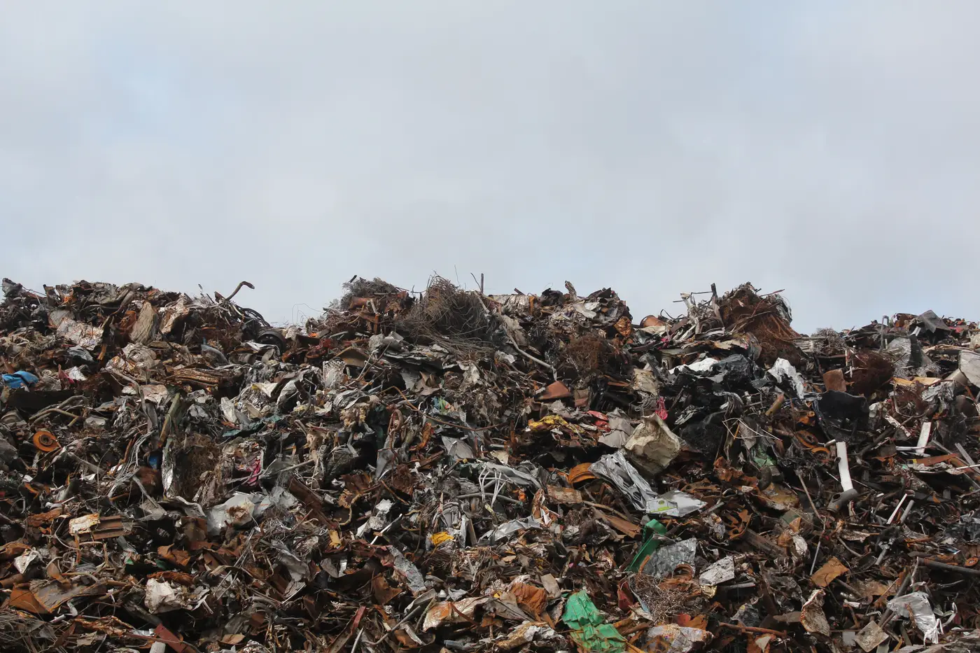 A mounded pile of mixed scrap metal, much of it rust-brown and weathered, under an overcast sky.